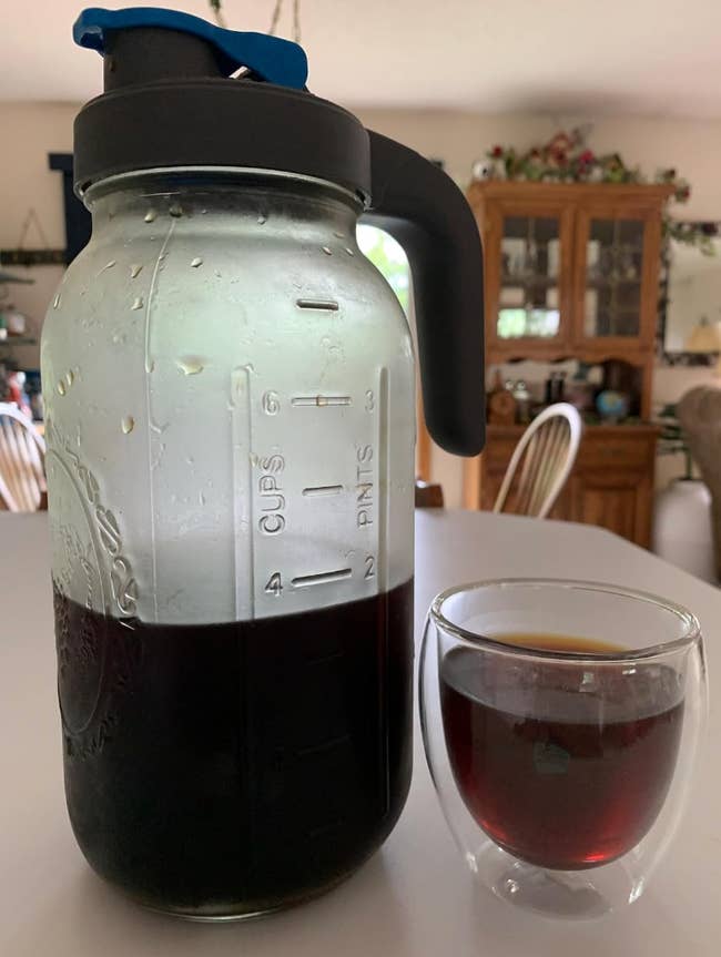 clear handled pitcher of cold brew coffee next to a cup with coffee poured into a 