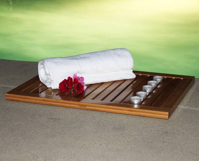 Bamboo bath tray with a rolled white towel, red flowers, and five small candles, suggesting a spa-like, relaxing ambiance