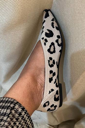 Person wearing leopard print flats and plaid pants, showcasing a stylish shoe choice on a fabric background