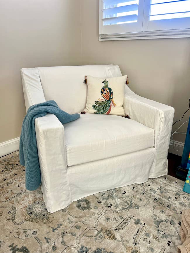 An armchair with a floral vertebrate pillow and a folded broad connected the armrest, acceptable successful a surviving country with a patterned rug