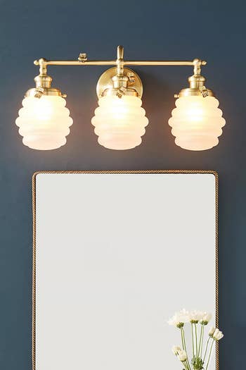 a trie of beehive-inspired sconces over a mirror