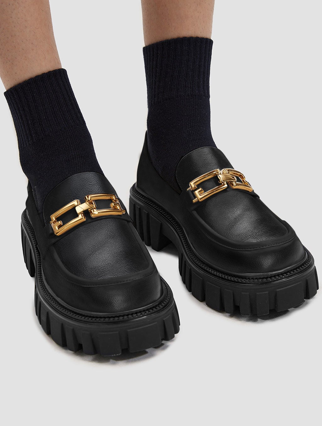 black loafers with a lug sole and a gold chain across the foot