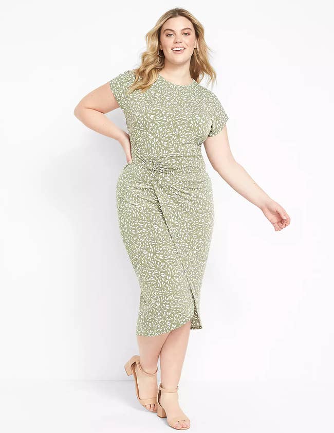Model is wearing a pale green body con wrap dress with a white leaf pattern throughout and nude heels