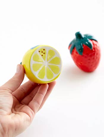 Hand holding a lemon-shaped squeezer with a strawberry-shaped squeezer in the background