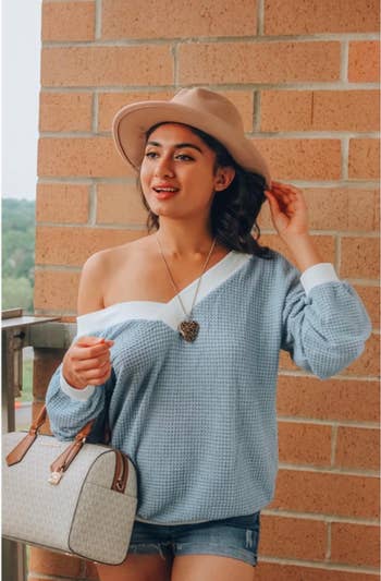 the reviewer wearing the sweater off the shoulder with a fedora and handbag