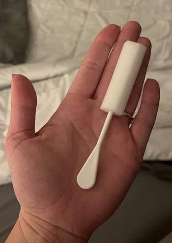 Hand holding a white foam and plastic sponge stick