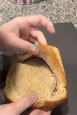 Person peels apical  crust disconnected  a portion    of brownish  bread, revealing a bladed  furniture   of filling inside