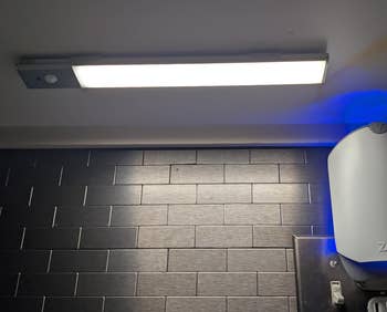 A sleek, modern   under-cabinet LED airy  fixture installed supra  a acheronian  tiled backsplash, adjacent  to a tiny  appliance. Ideal for room  lighting