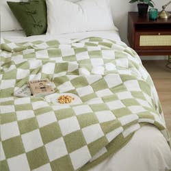 A bed with a green and white checkered blanket, a book, and a bowl of snacks on top