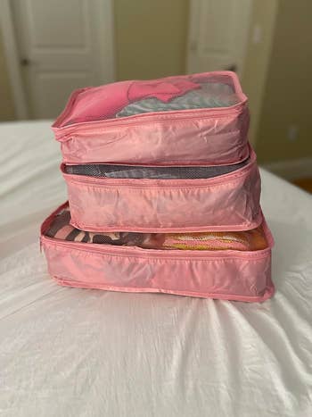 pink packing cubes stacked on a bed