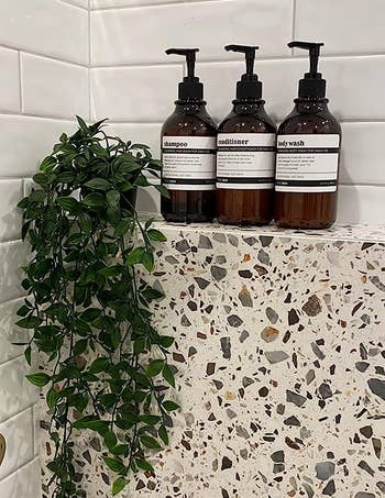 Reviewer's shampoo, conditioner, and body wash bottles are shown on the wall of a shower