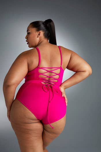 front of a model wearing a hot pink one-piece, showing off the lace-up back