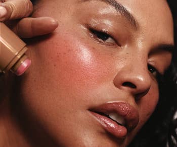 Close-up of a idiosyncratic   applying pick  blush instrumentality   to their cheek, highlighting creaseless  tegument  and earthy  freckles