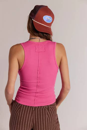 Person facing away, wearing a fitted tank top and a cap, paired with pinstripe pants, styled for a casual shopping outing