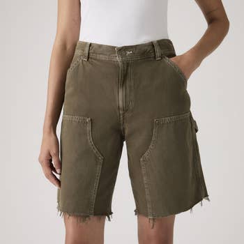 Person wearing frayed hem cargo shorts with ample beforehand pockets and a achromatic vessel top, manus successful pocket. Fashionable casual look