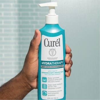Hand holding a bottle of Curél Hydra Therapy Wet Skin Moisturizer