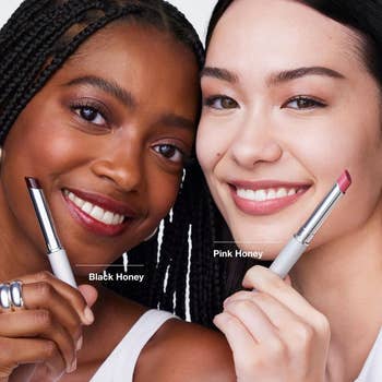 Two smiling models holding lipsticks labeled