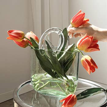 Clear handbag utilized  arsenic  a vase with tulips and a manus  adjusting flowers, placed connected  a solid  table