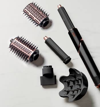 Assorted hair styling tools including a blow dryer, curling wands, and brushes on a marble surface