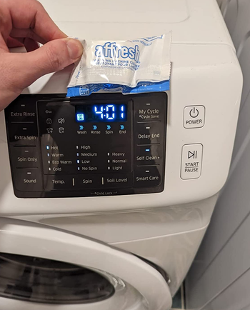 reviewer holding a cleaning tablet in front of a washing machine