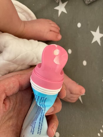 A reviewer holding a bottle of cream with the pink attachment and some of the cream coming out the top