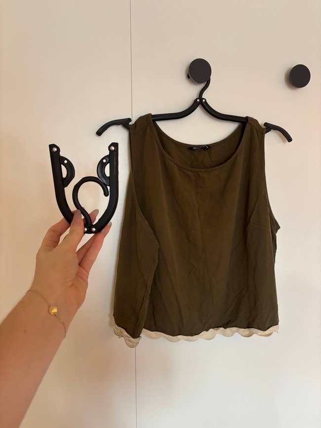 A sleeveless top hangs on a stylish modular hanger held by a hand, showcasing its functionality for organizing clothing
