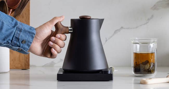 person reaching for the matte black and wood-handled electric kettle