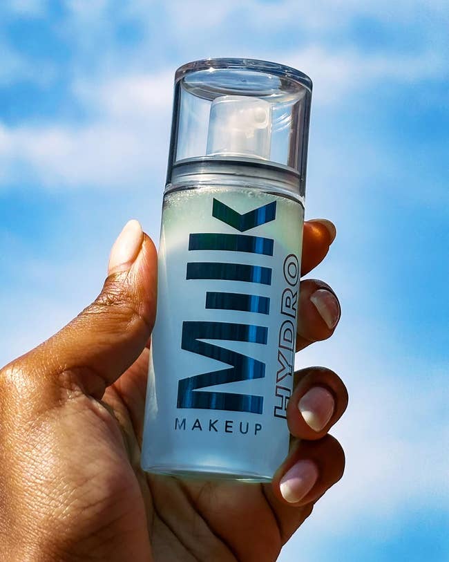 model holding a vessel of Milk Makeup Hydro mounting spray against a bluish entity background