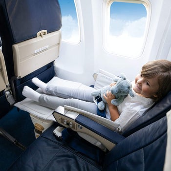 child model sitting in a plane seat and using the suitcase as a leg rest