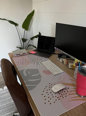 Home office desk with a laptop, monitor, mouse on top a pastel mat with a minimalist print 