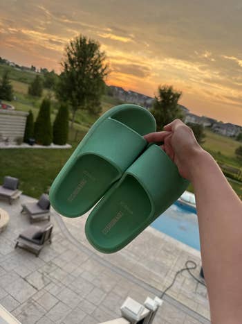 A manus  holds greenish  slides outdoors with a excavation  and sunset successful  the background