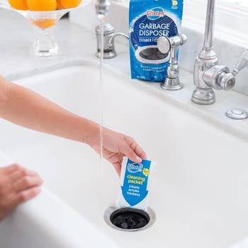 hand placing the garbage disposal cleaner packet into a drain