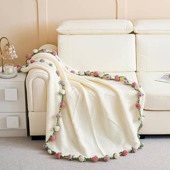 Cozy cream throw blanket with a decorative floral border draped over a white sofa in a modern living room setting