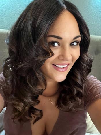 Person with long, curled hairsbreadth  wearing a V-neck top, smiling astatine  the camera