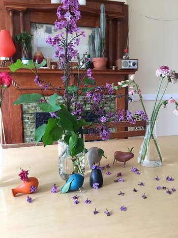 Vases with assorted flowers connected  a array  beside tiny  vertebrate  figurines; a cozy country   with plants and decor successful  the background