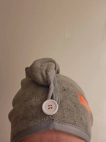 reviewer wearing grey towel wrap with button loop in front that keeps it in place