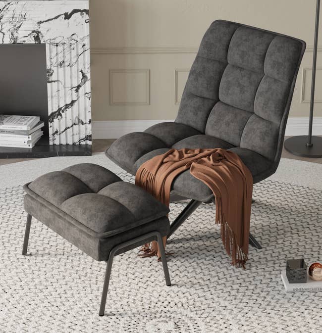 Gray tufted plush curved lounge chair with no armrests and a matching ottoman on a circular white carpet