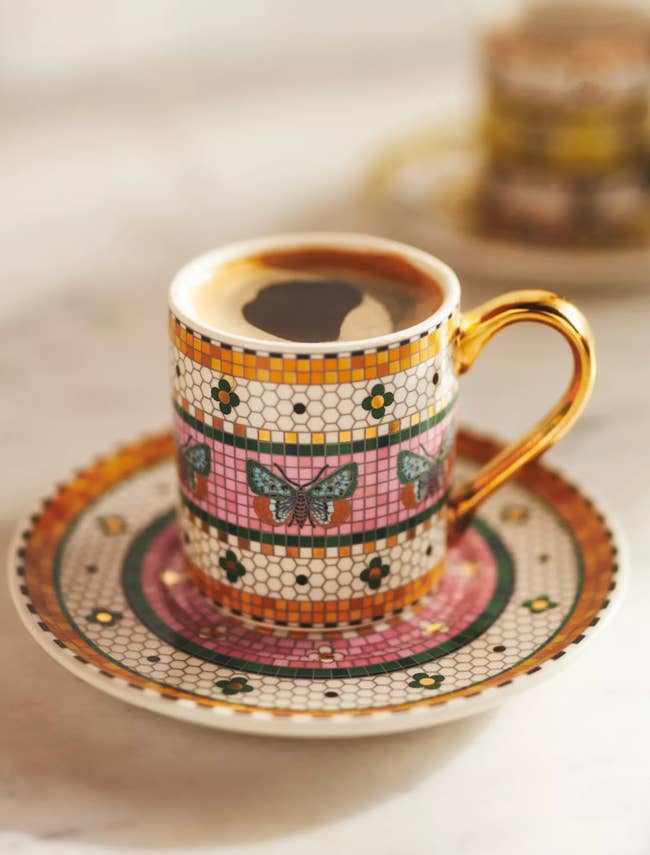 Elegant java cupful with a golden handle, decorated with butterflies and floral patterns, matching saucer successful a shopping-focused article