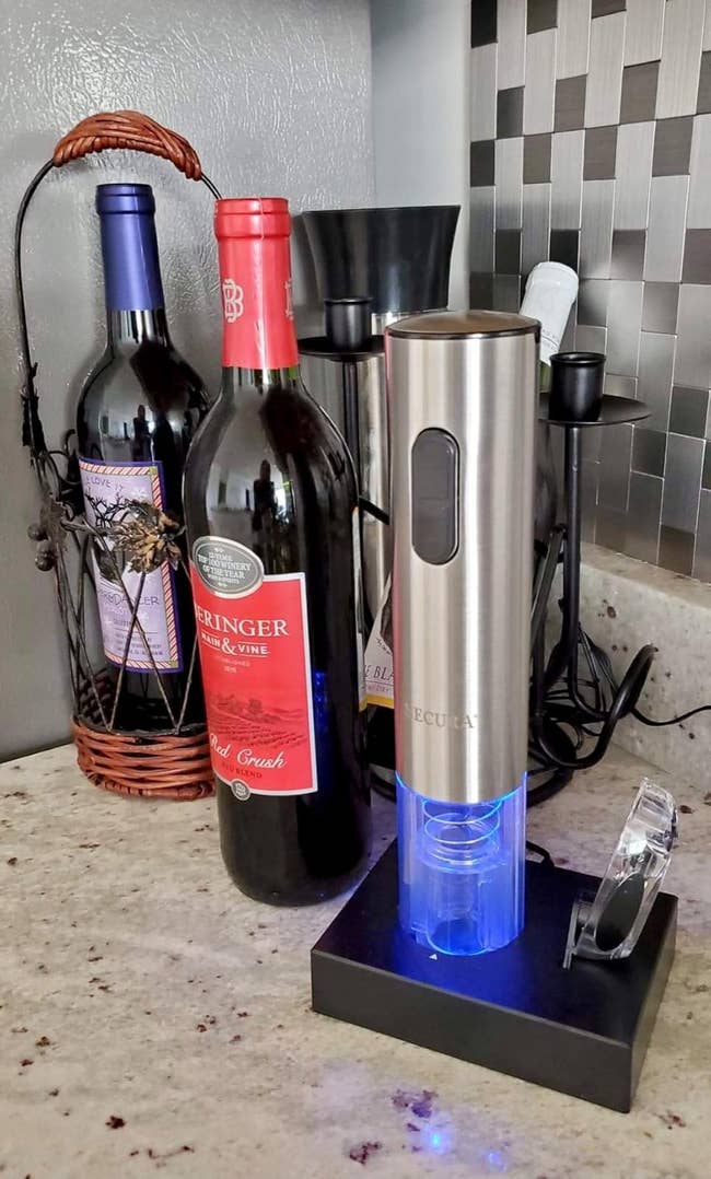 Electric wine opener on a counter next to bottles of wine, featuring a sleek metallic design with a glowing base