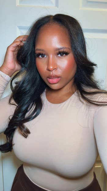 Person posing indoors with long, styled hair, wearing a fitted long-sleeve top