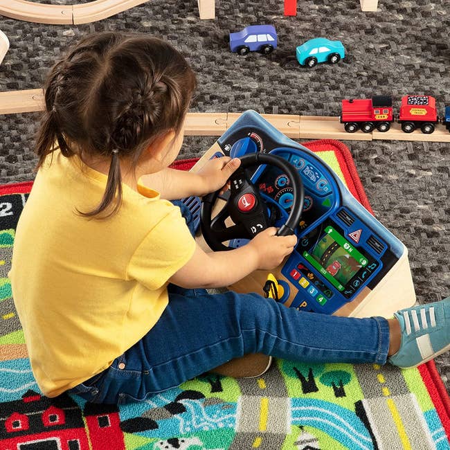 child playing with wooden steering wheel toy on a play mat
