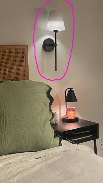 A modern   chamber  setup with a wall-mounted sconce lamp, a greenish  pillow, and a nightstand.