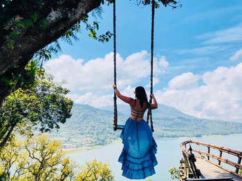 A reviewer in the backless dress on a swing overlooking the water