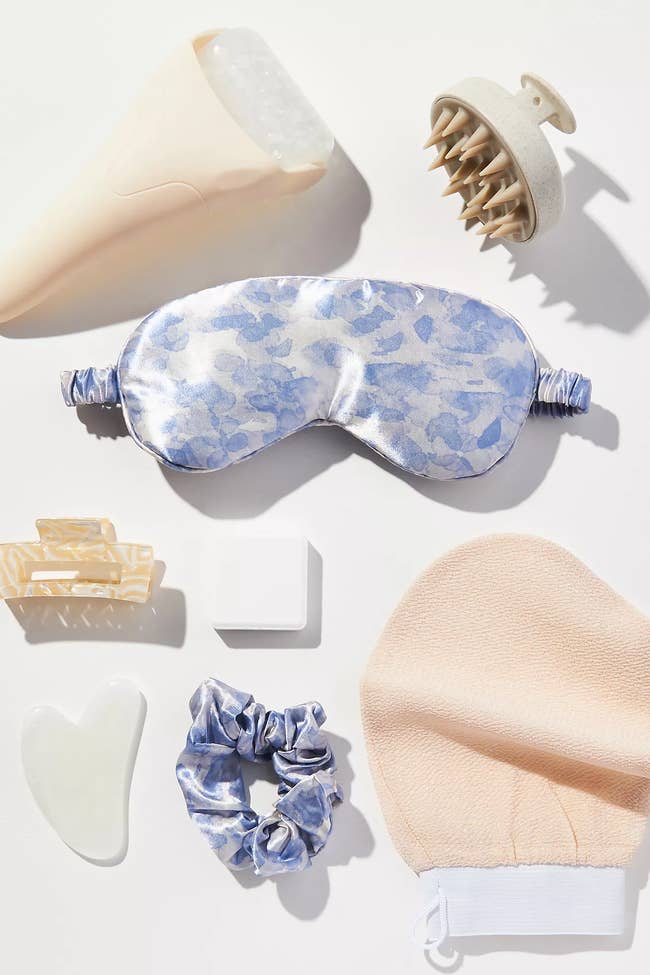 Variety of self-care items including an crystal roller, silk oculus mask, scalp massager, hairsbreadth clip, scrunchie, exfoliating mitt, and a chromatic gua sha