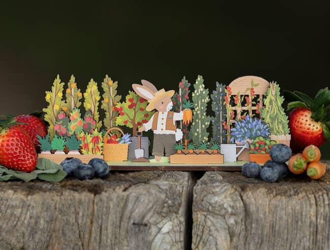 Handcrafted paper display featuring a rabbit gardener with baskets beside fresh strawberries and blueberries on wood
