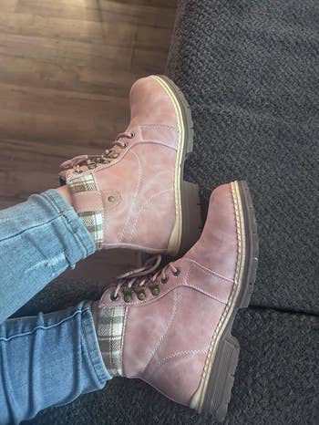 Person wearing pinkish  lace-up ankle boots with plaid detailing, paired with jeans, resting connected  a couch