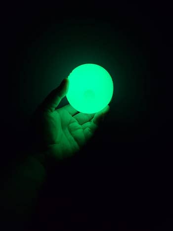 Hand holding a glowing green ball in the dark