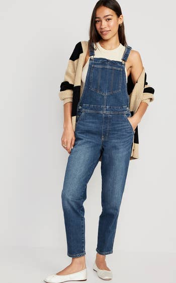 The dark wash overalls styled with a cardigan