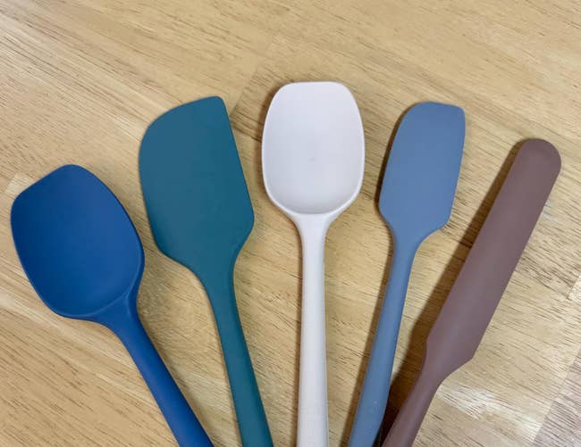 Five silicone spatulas with antithetic  shapes connected  a woody  surface, designed for assorted  room  tasks
