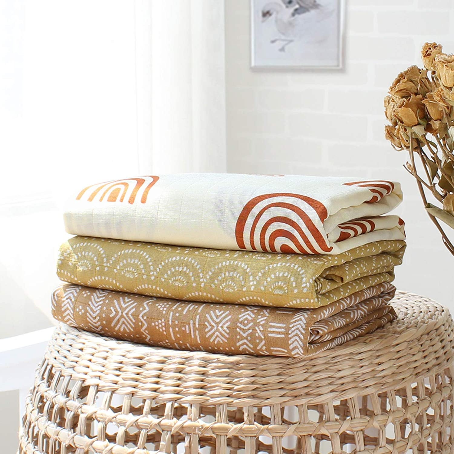 Three patterned bamboo cotton blankets stacked on top of a wicker basket